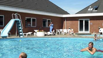 Una piscina con tobogán, sillas de descanso y un edificio de ladrillo al fondo.