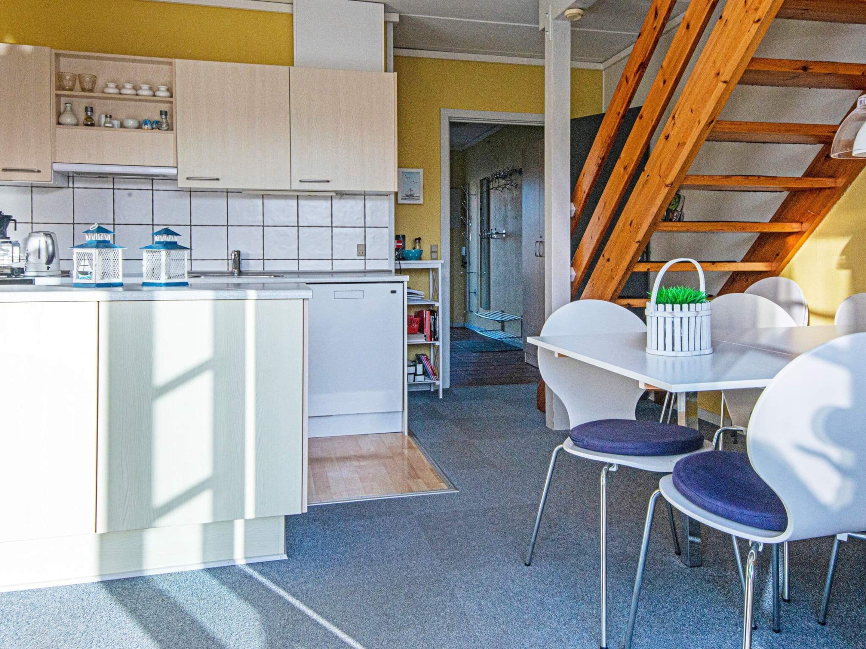 A modern kitchen with white cabinets, a central island, and a dining area with white chairs and a table.