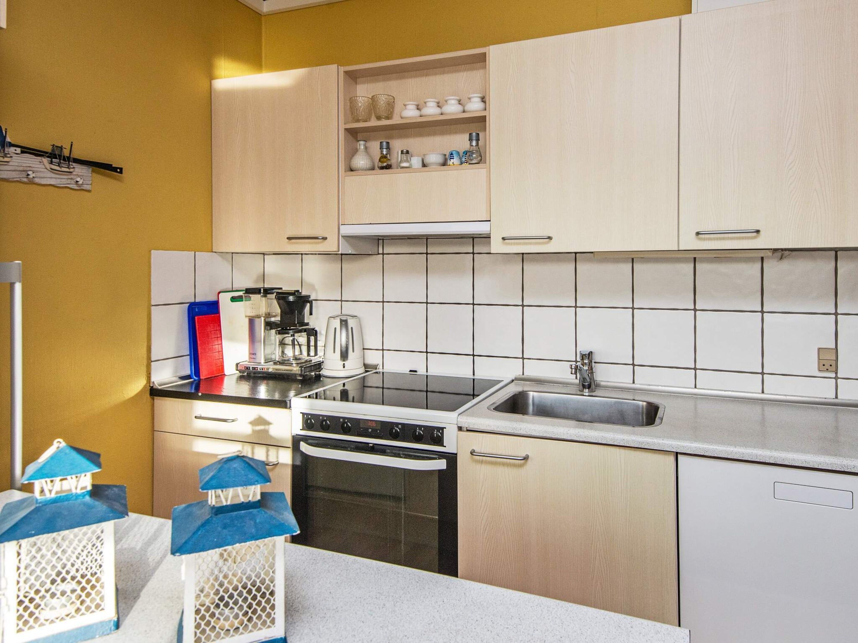 A kitchen with white cabinets, a black stove, a sink, and a coffee maker.