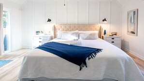 Un grand lit recouvert d’une couvre-lit blanche et bleue, deux tables de chevet et une petite table de nuit avec une lampe.