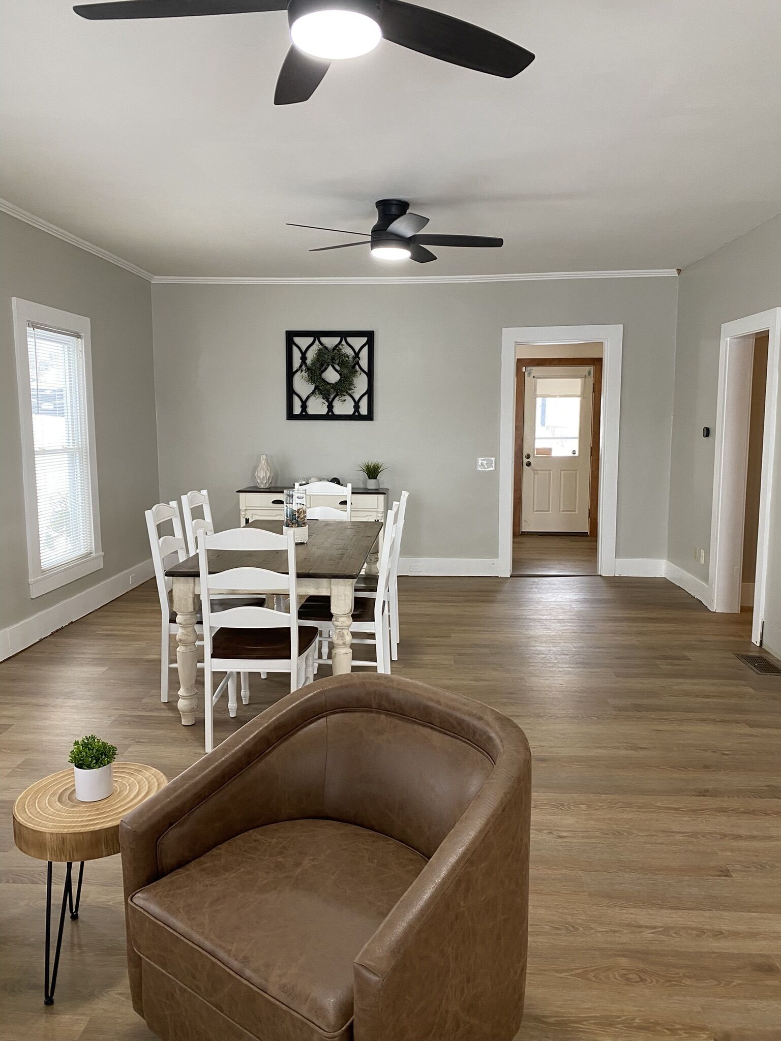 Un espacio habitable amplio con una mesa de comedor, sillas blancas, un sofá de cuero marrón y un ventilador de techo.