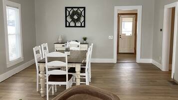 Un espacio habitable amplio con una mesa de comedor, sillas blancas, un sofá de cuero marrón y un ventilador de techo.