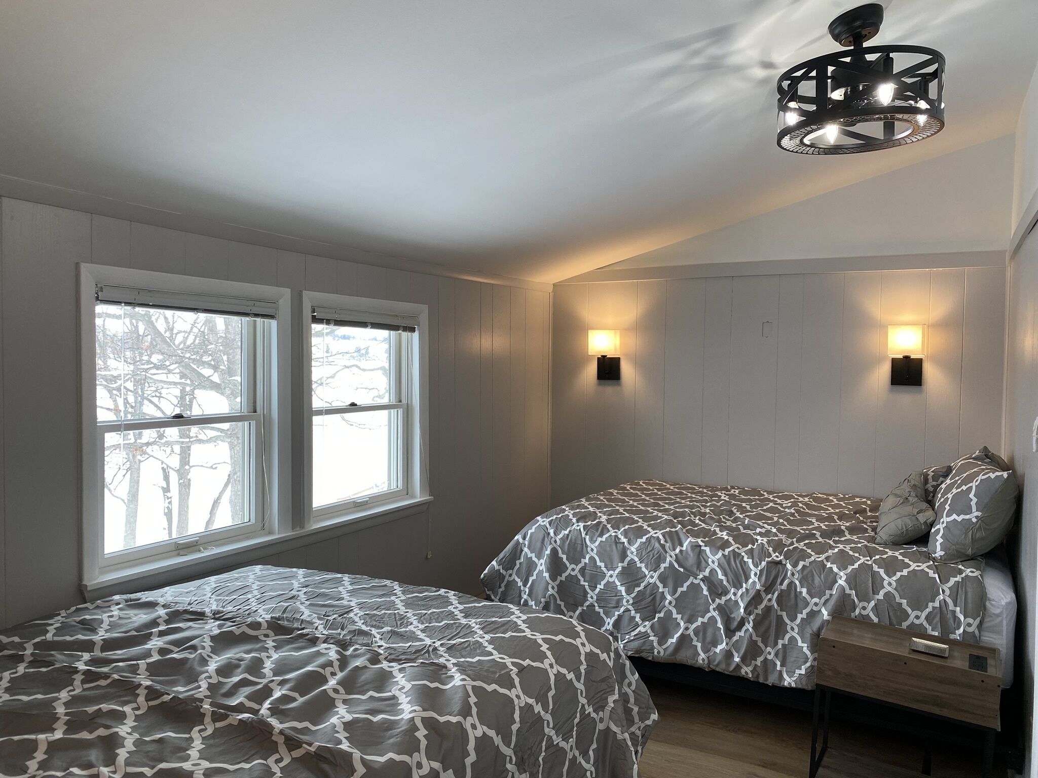 Un dormitorio con dos camas, una ventana e iluminación en la pared.