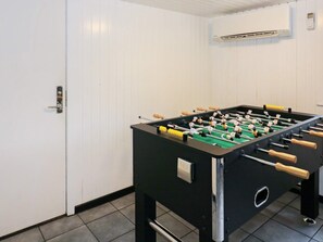 A room with a foosball table, a door, and an air conditioning unit on the wall.