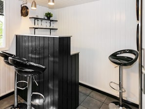 A bar area with two black bar stools, a shelf with wine glasses, and a hanging light fixture. - 4 Star Holiday Home in Hadsund (Hadsund)