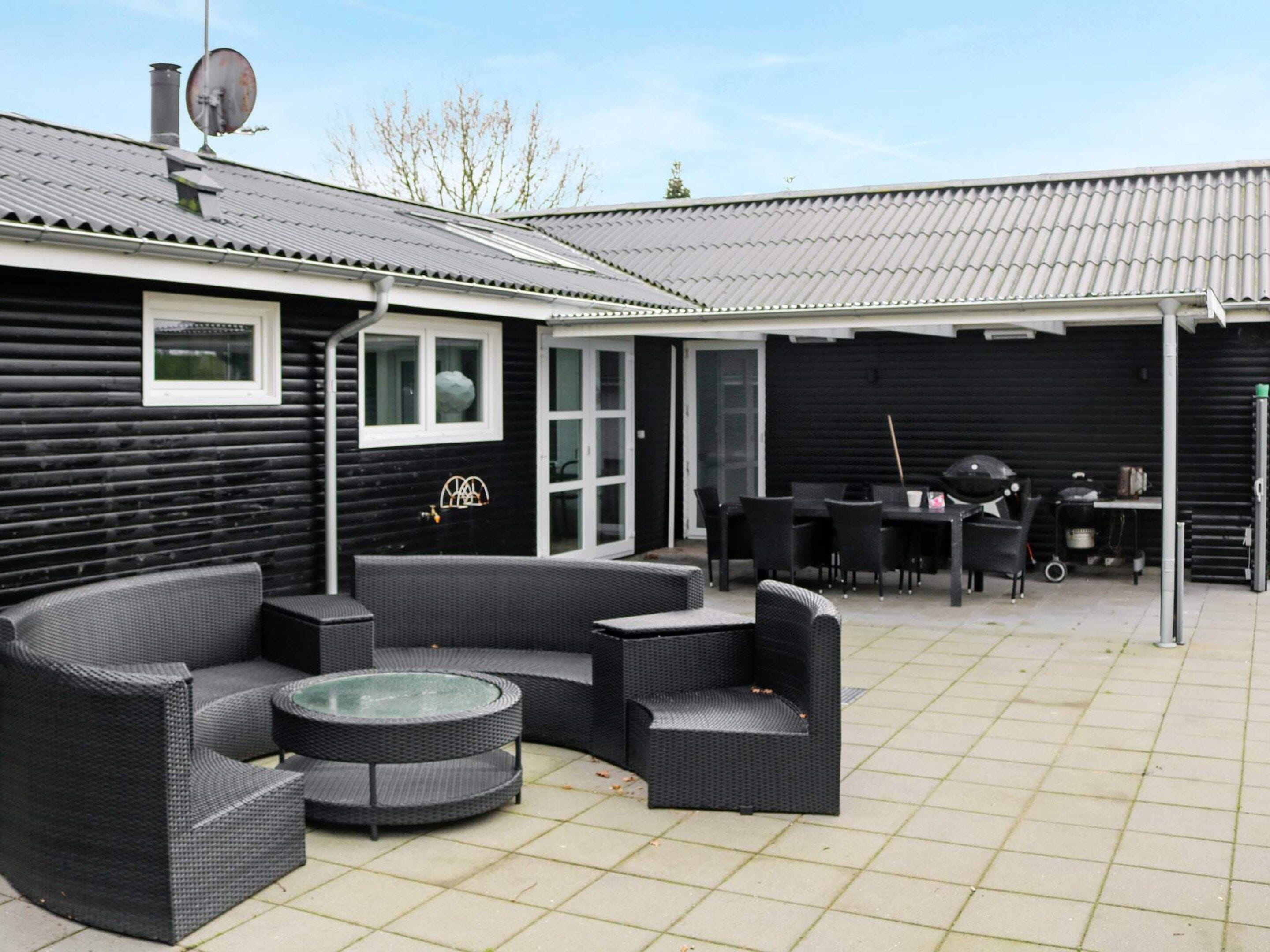 A covered outdoor patio with a round table and multiple chairs, a grill, and a dining table with chairs.