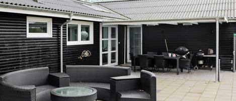 A covered outdoor patio with a round table and multiple chairs, a grill, and a dining table with chairs.