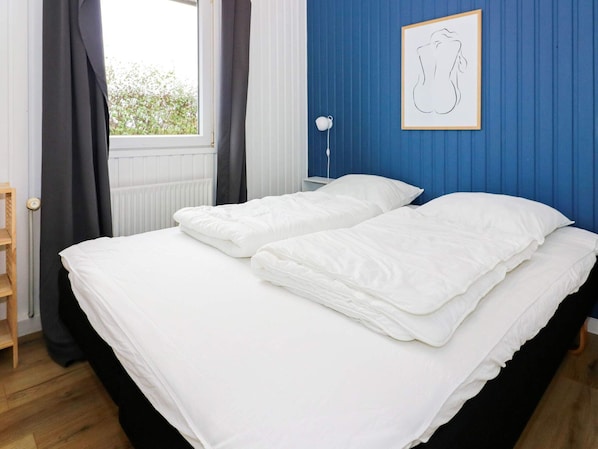 A bedroom with a bed, a window with curtains, a radiator, and a framed picture on the wall.