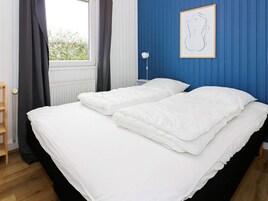 Un dormitorio con cama, ventana con cortinas, radiador y un cuadro en la pared.