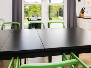 A dining area with a black table and green chairs, a window with a view of a garden, and a kitchen area with a knife block.