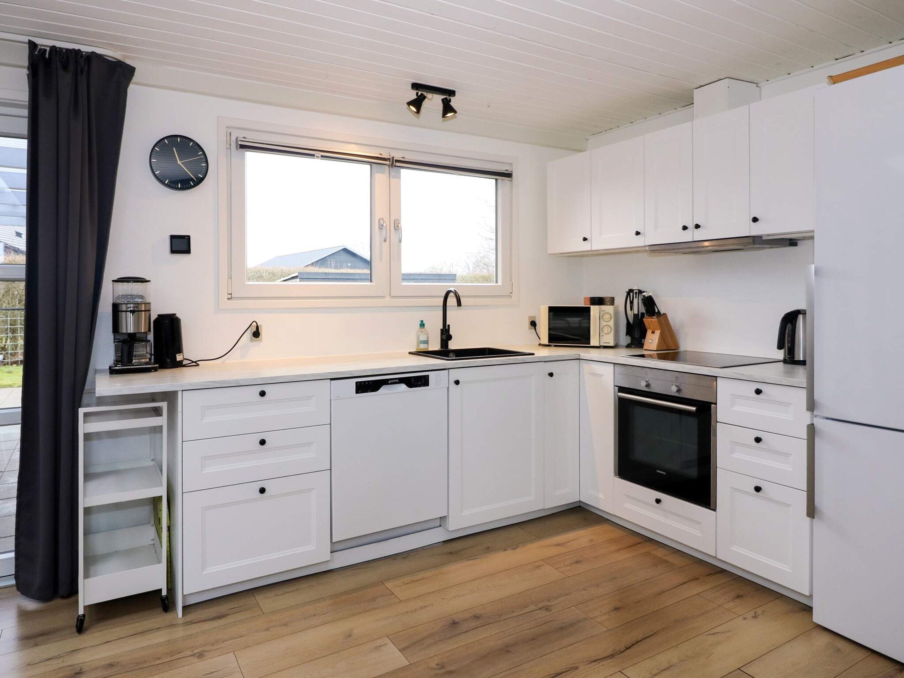 A modern kitchen with white cabinetry, a built-in oven, a microwave, and a coffee maker.