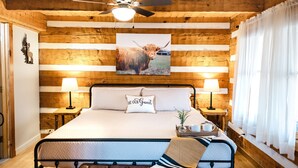 Un dormitorio de estilo cabaña de madera con una cama, dos lámparas de noche, un ventilador de techo y un cuadro de un toro en la pared.