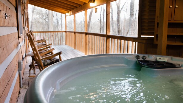 Una cabaña de madera con jacuzzi, terraza de madera y vista a árboles.