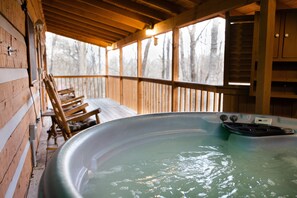 Una cabaña de madera con jacuzzi, terraza de madera y vista a árboles.
