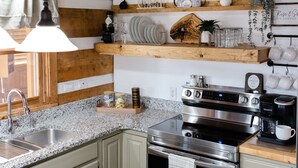 Una cocina con encimeras de granito, estufa de acero inoxidable y estantes de madera sobre el fregadero.