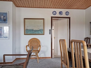 Ein Zimmer mit einem Esstisch, zwei Stühlen, einem Korbstuhl, einem Gemälde eines Schiffes an der Wand und drei blau-weißen Tellern über der Tür.