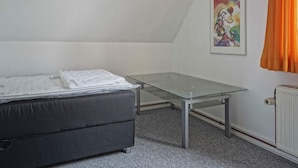 A small, sparsely furnished room with a bed, a glass table, a radiator, and a painting on the wall. - 8 Person Holiday Home in Hasle (Hasle)