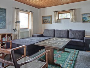 A cozy room with a sofa, a wooden table, and a chair. There are bookshelves and a lamp. - 8 Person Holiday Home in Hasle (Hasle)