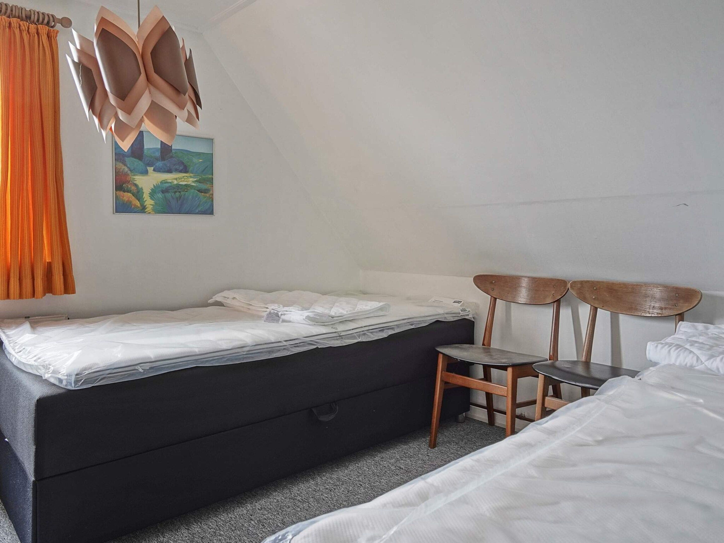 Una stanza con un letto, una sedia, una scrivania e un quadro appeso al muro.