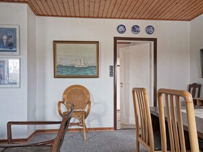 A room with a dining table, two chairs, a wicker chair, a painting of a ship on the wall, and three blue and white plates above the door. - 8 Person Holiday Home in Hasle (Hasle)