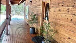 Een houten chalet met een overdekte veranda, bloempotten en een deur met een raam.