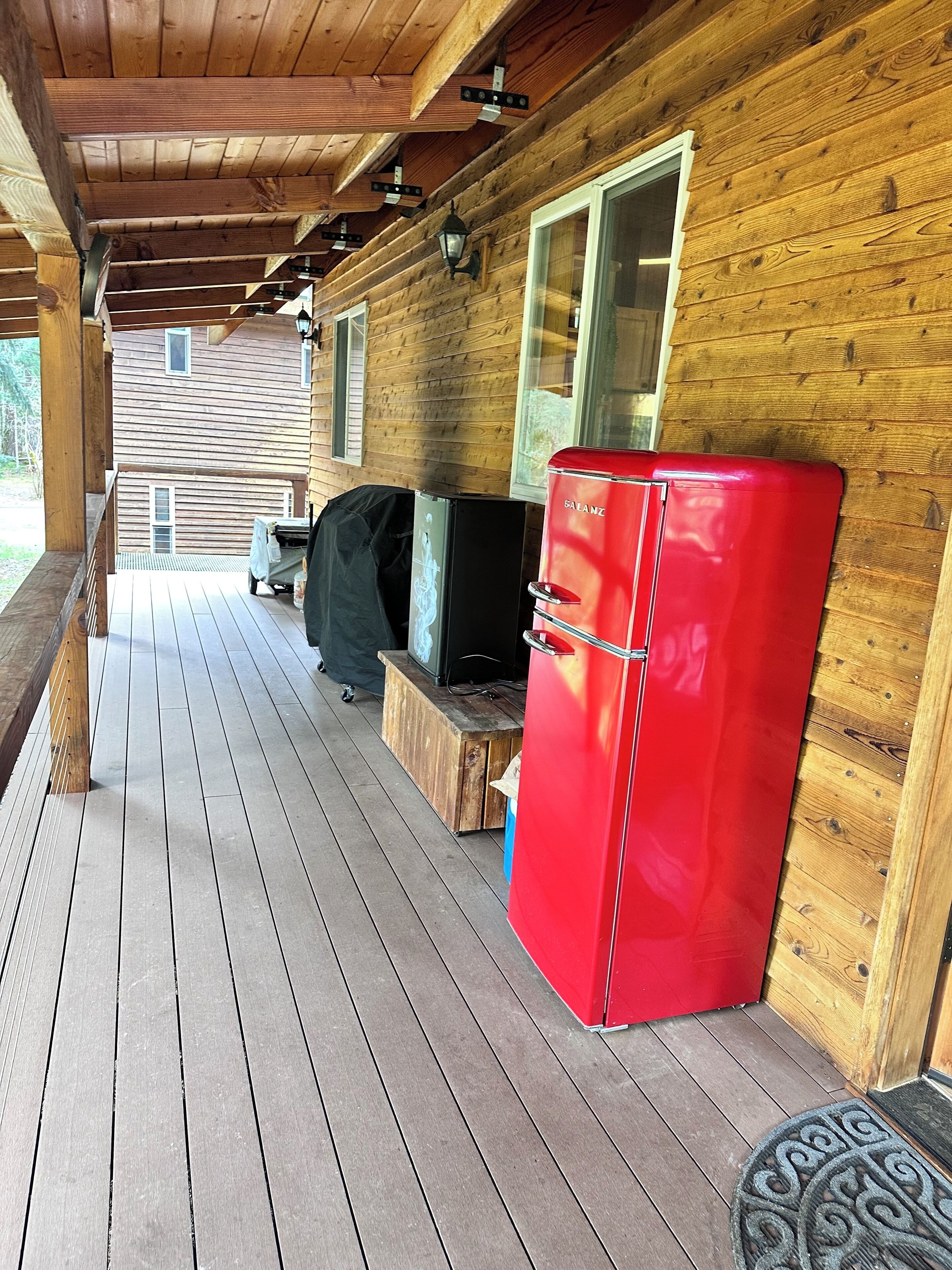 En træhytte med veranda, et rødt køleskab og en grill.