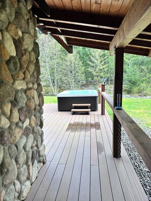 Une terrasse en bois avec un muret en pierre, un jacuzzi et un banc.