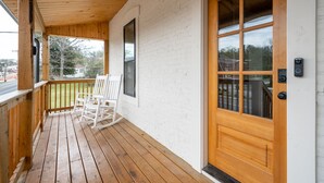 A wooden porch with a white brick wall, a wooden door with glass panels, and a white rocking chair.