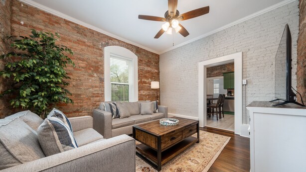 A living room with a brick wall, a ceiling fan, a sofa, a coffee table, and a rug.