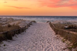 Ein Sandweg am Strand, der zum Meer führt, mit einem Holenzaun auf beiden Seiten.