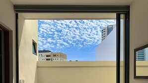 A modern room with a large sliding glass door leading to a balcony. The room has a tiled floor and a plain wall. - NEW! Ample Condo- Walk to Beach! AMAZING Location! Everything Walk-in distance! (Mazatlán)