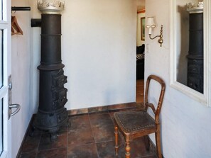 A narrow hallway with a large black stove, a wooden chair, and a white wall with a mirror.