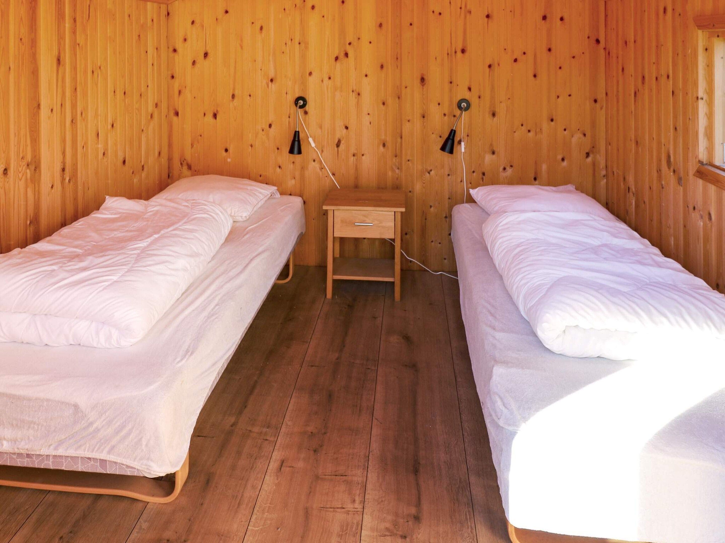 Une chambre avec deux lits simples, une petite table de chevet en bois et une lampe fixée au mur.