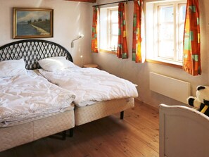 A room with two beds, a wooden floor, a painting on the wall, and a window with curtains.