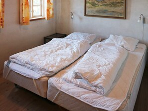 A double bed with a quilted mattress and pillows, a bedside table, a wall-mounted lamp, and a painting above the bed. - 4 Star Holiday Home in Hadsund (Hadsund)