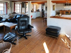 A spacious living area with a leather sofa, a dining table, and a kitchen in the background. - 4 Star Holiday Home in Hadsund (Hadsund)
