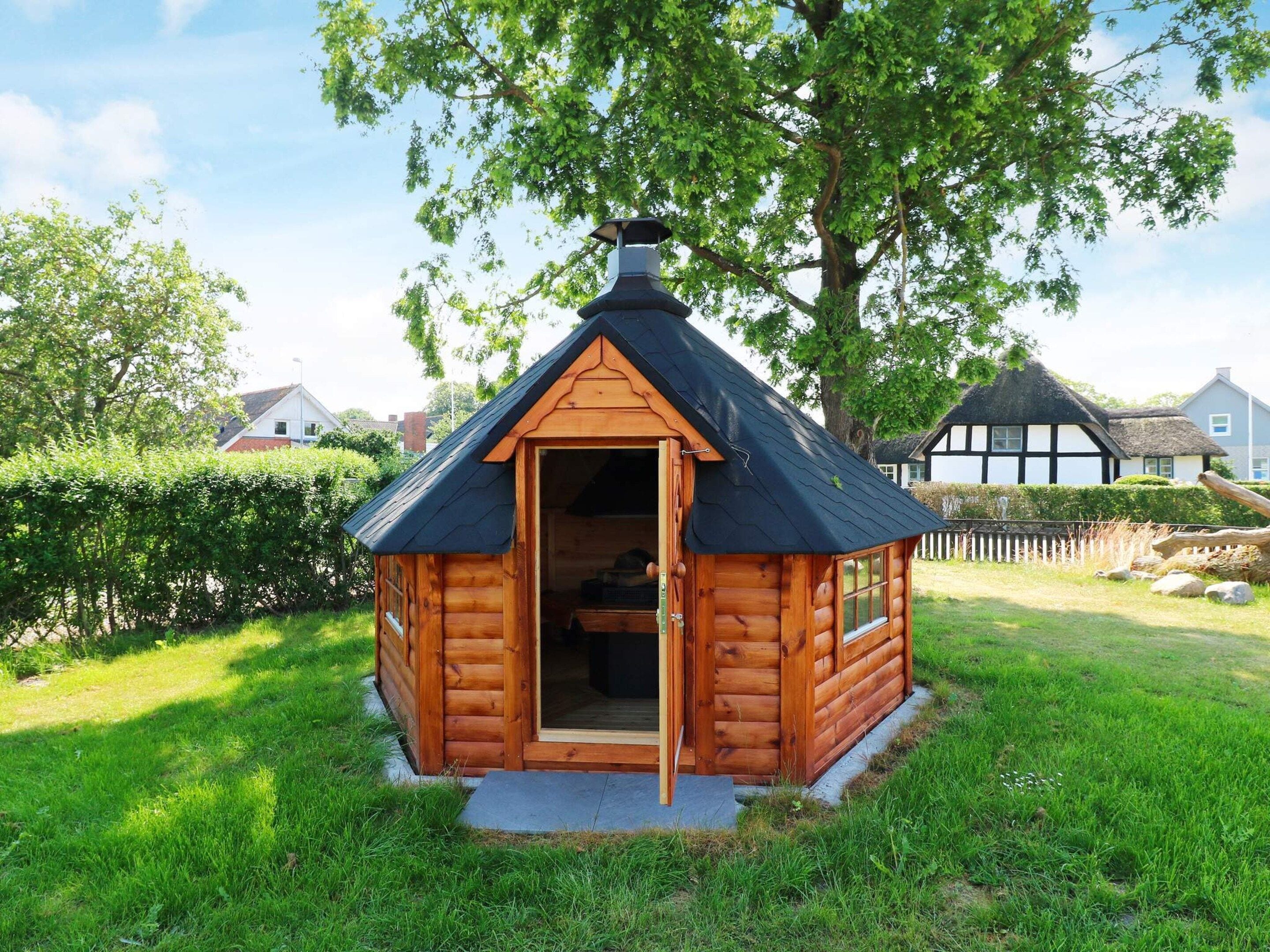 Una cabaña de madera con techo de paja, una chimenea y una puerta que da al interior.