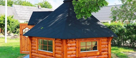 A wooden cabin with a black roof, a chimney, and a window.