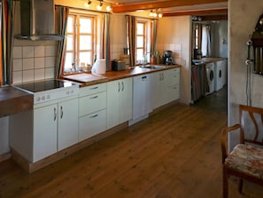 Une cuisine avec des meubles blancs, un plan de travail en bois, une cuisinière et un lave-linge à l’arrière-plan.