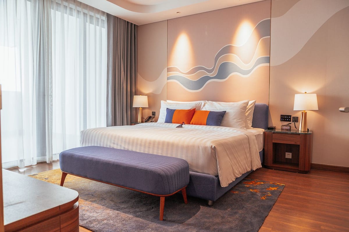 A modern hotel room with a large bed, a bench, a nightstand, and a desk.