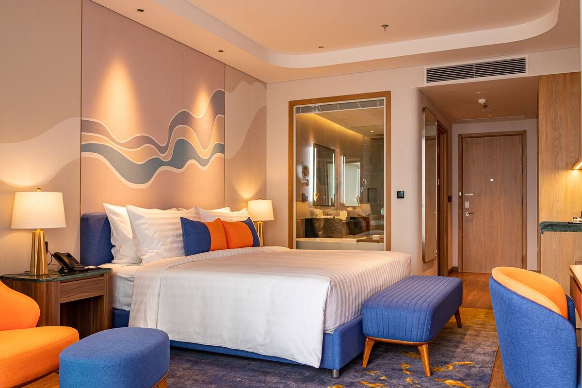 A hotel room with a large bed, two bedside tables with lamps, a seating area with chairs, and a mirror.
