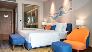 A modern hotel room with a large bed, two bedside lamps, a blue and orange armchair, and a wooden floor. - Dream Dragon Resort (Hai Phong)