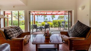 A room with two leather sofas facing a glass door leading to a patio with a view of the ocean. - Malaqereqere Villas Ocean/Pool View, Villa 3 (Sigatoka)