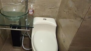 Une salle de bain avec un lavabo en verre, des toilettes blanches et un distributeur de savon.