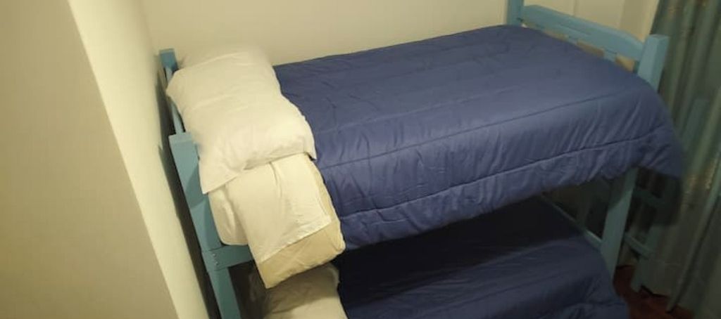 Ein Etagenbett mit blauer Matratze und weißem Kopfkissen.