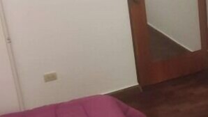 Une pièce avec une porte en bois, un miroir et un lit recouvert d’une couverture rose.