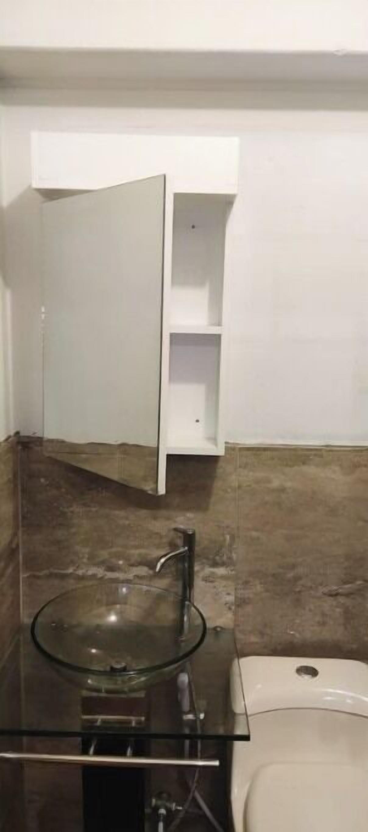 Un baño con un lavabo de vidrio, un inodoro blanco y un armario blanco con puertas abiertas.