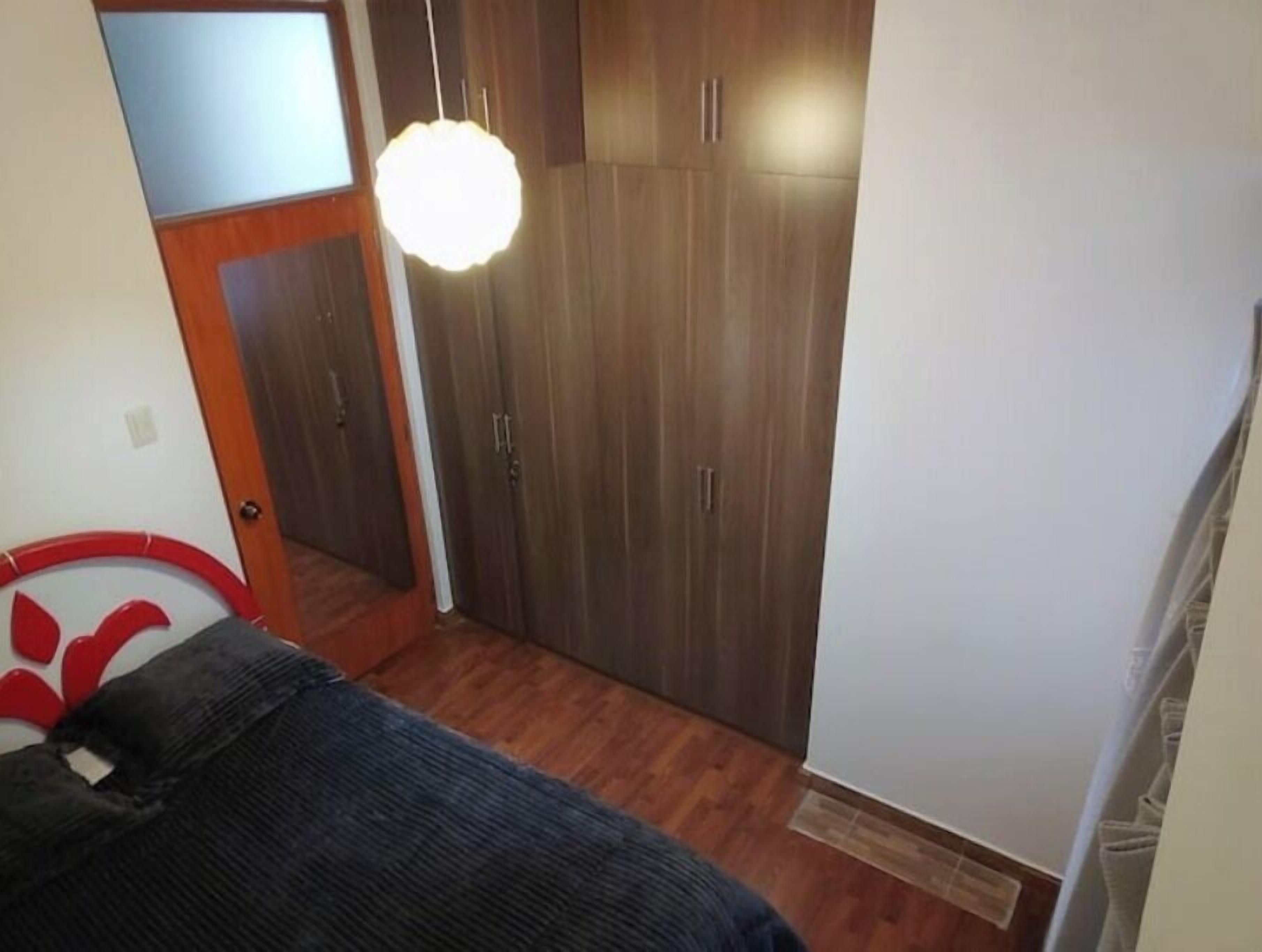 A bedroom with a bed, wooden wardrobe, and a hanging light fixture.