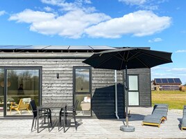 Un edificio moderno con grandes ventanales, una terraza amoblada y paneles solares al fondo.