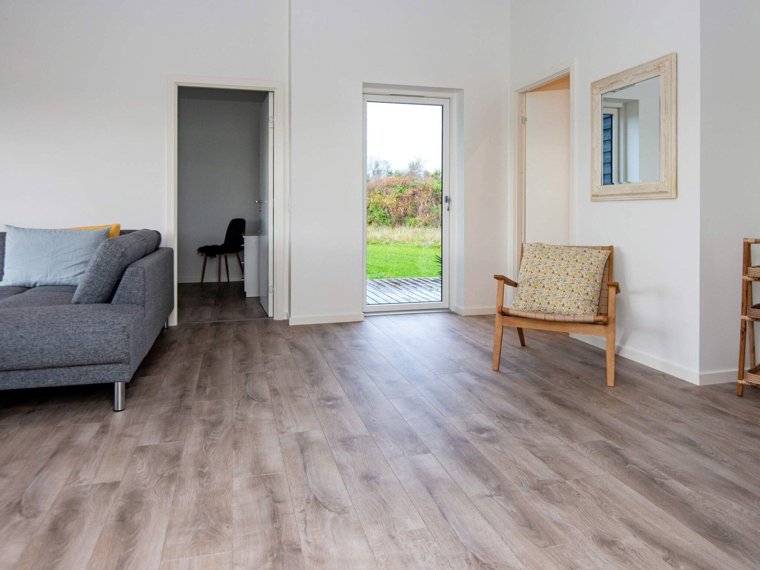 A modern living room with a grey sofa, a wooden chair, and a door leading to a balcony.